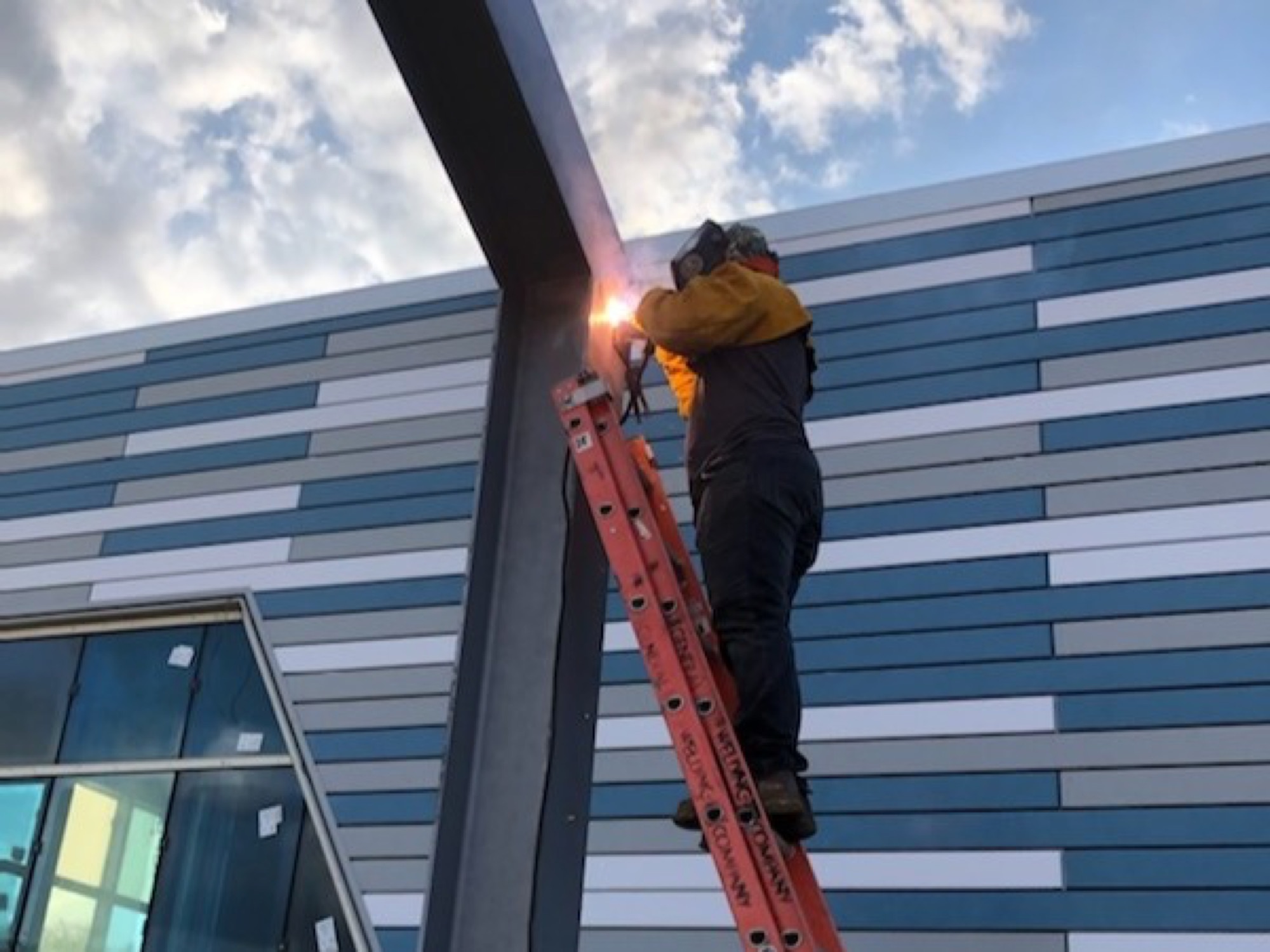 GWC welder on a ladder welding a steel column on a building exterior